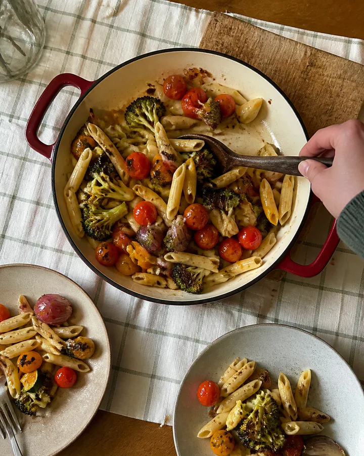 Customer serving pasta and roasted vegetables from a red skillet